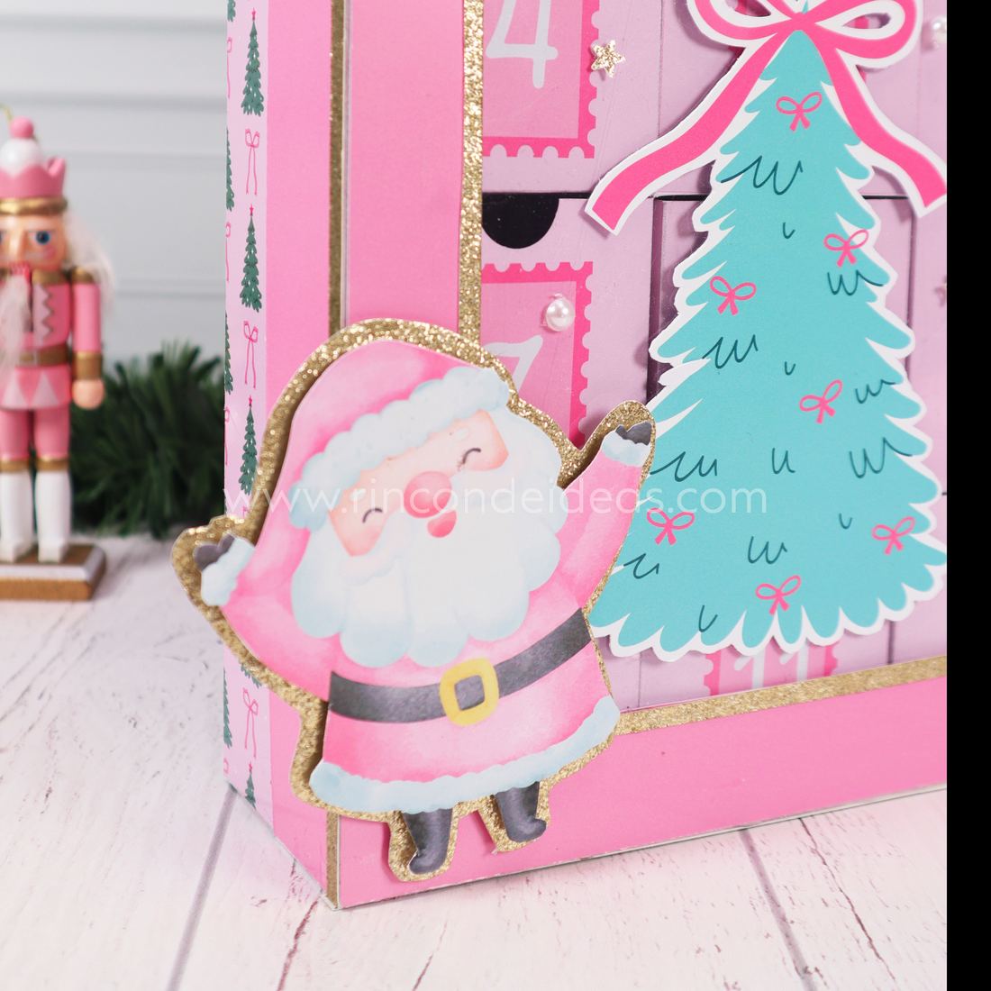 Detalle del calendario de Adviento: Papá Noel rosa con borde de glitter dorado y árbol verde agua con moños · Masterclass de Navidad 2026