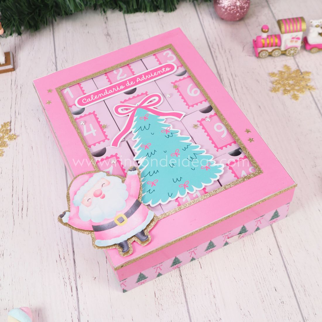 Calendario de Adviento rosa visto desde arriba, con tapa con ventana y lateral de arbolitos y moños · Masterclass de Navidad 2026