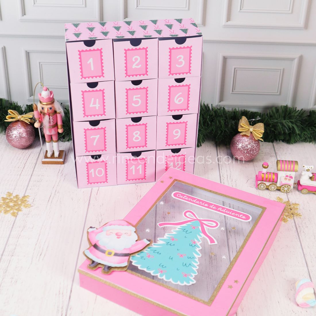 Doce cajitas numeradas rosas del calendario de Adviento paradas, con la tapa con árbol y Papá Noel adelante · Masterclass de Navidad 2026